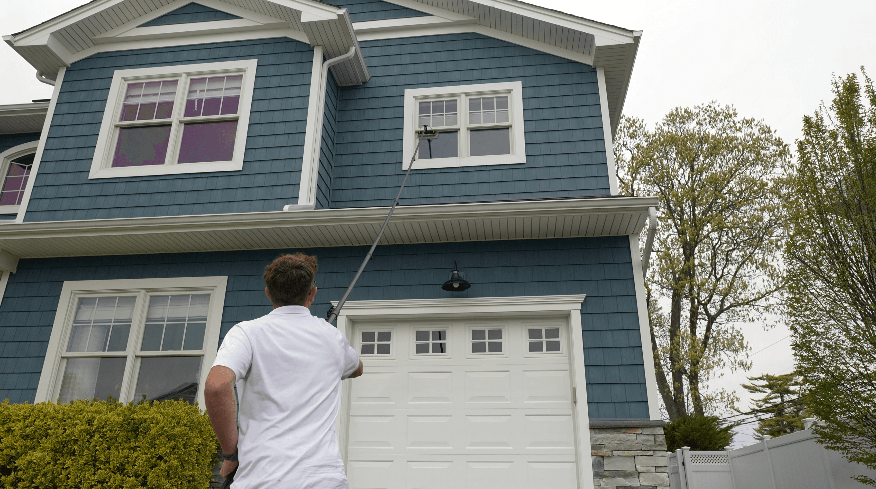 Technician cleaning upper-story windows with a water-fed pole on a Long Island home