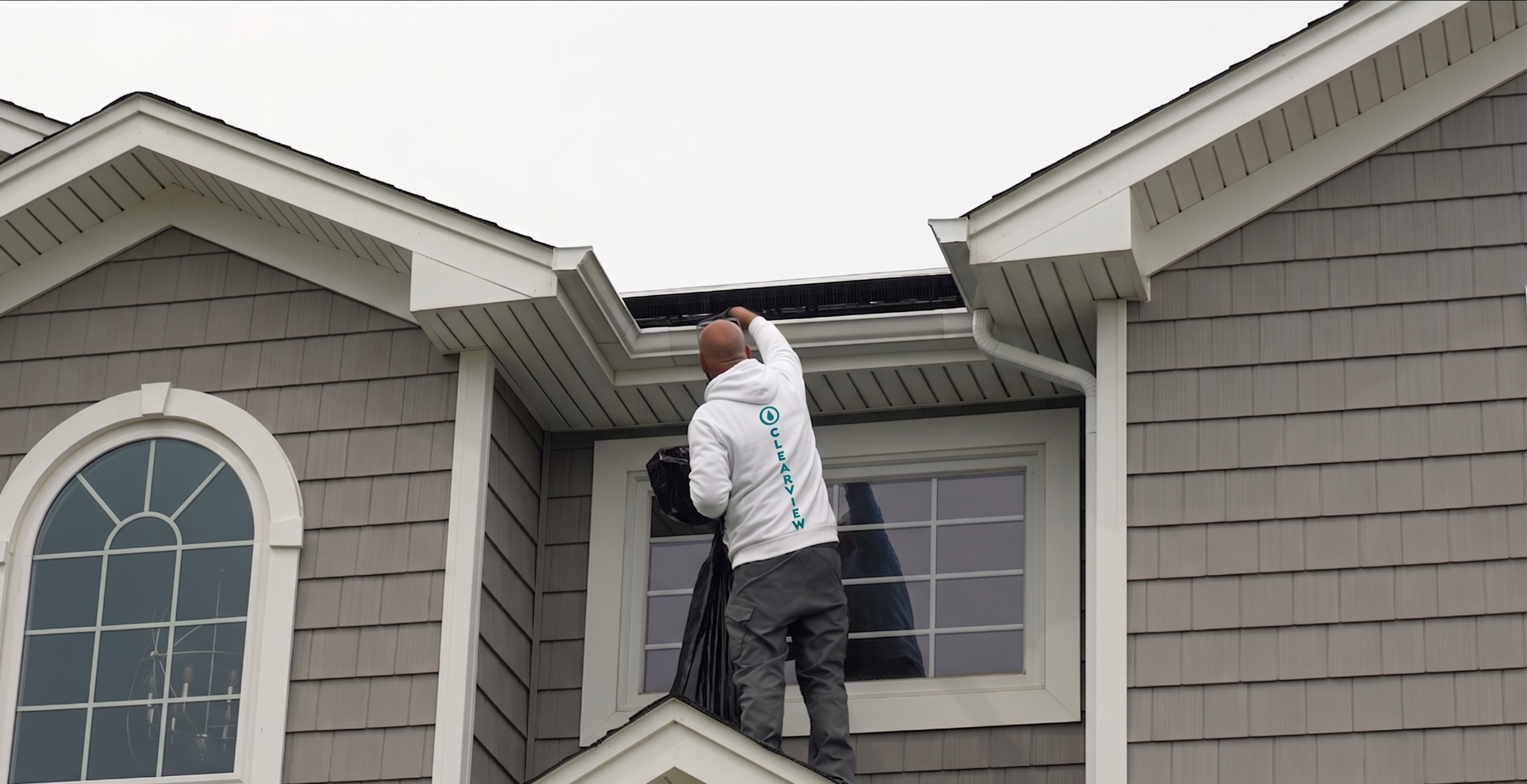 Gloved hands clearing wet leaves and debris from a white roof gutter
