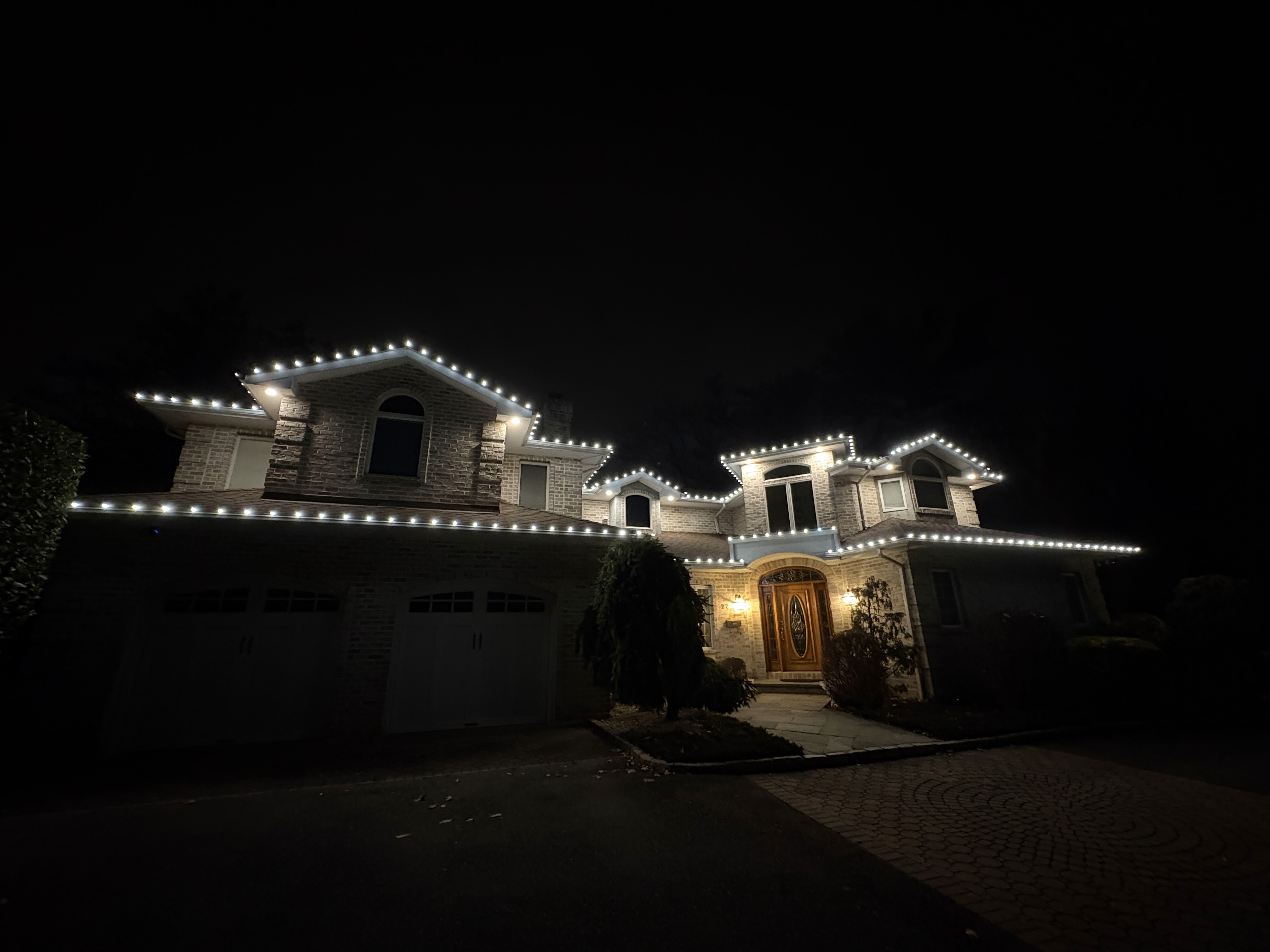 House decorated with warm white holiday lights along the roof, porch columns, and front walkway